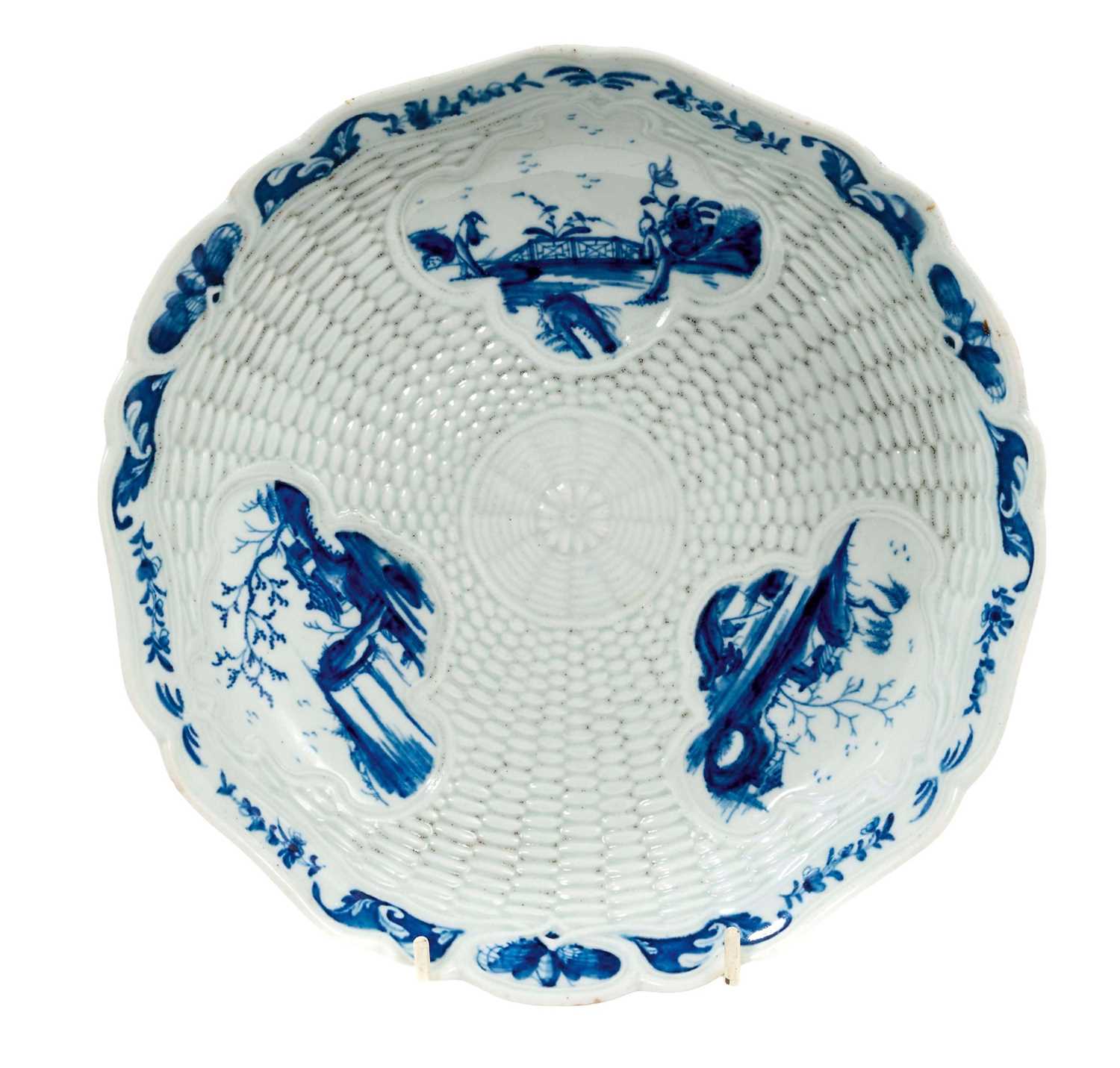 Lot 23 - Rare and early Worcester blue and white junket dish, circa 1758, painted with three landscape panels in the Neighbours pattern on a basket-weave moulded ground, the shaped rim with flowers and...