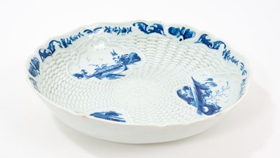 Lot 23 - Rare and early Worcester blue and white junket dish, circa 1758, painted with three landscape panels in the Neighbours pattern on a basket-weave moulded ground, the shaped rim with flowers and...