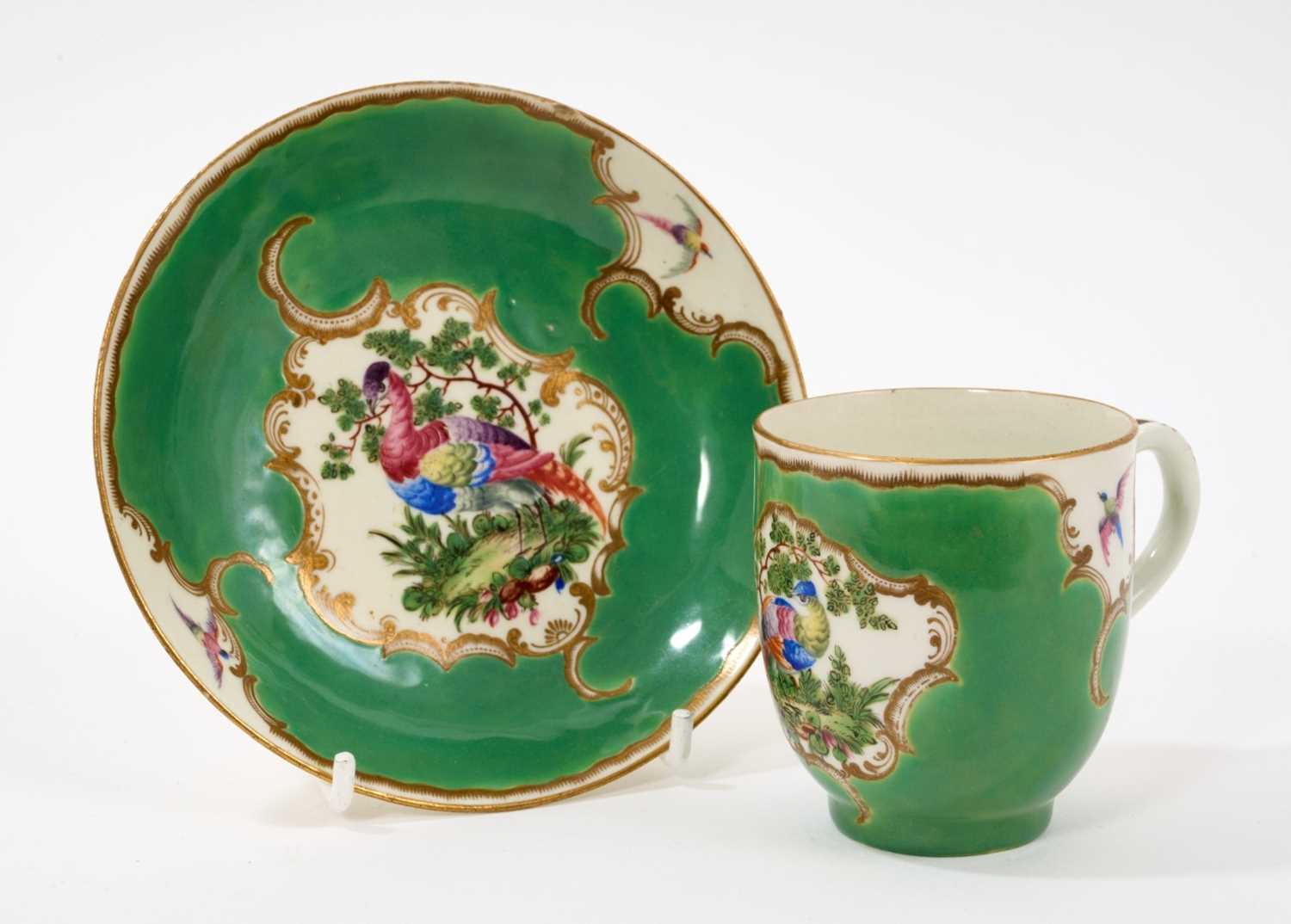 Lot 29 - A Worcester coffee cup and saucer, circa 1770, painted in coloured enamels with exotic birds, within gilt 'C' scroll cartouches, the apple-green ground with gilt scroll borders, panelled with sm...