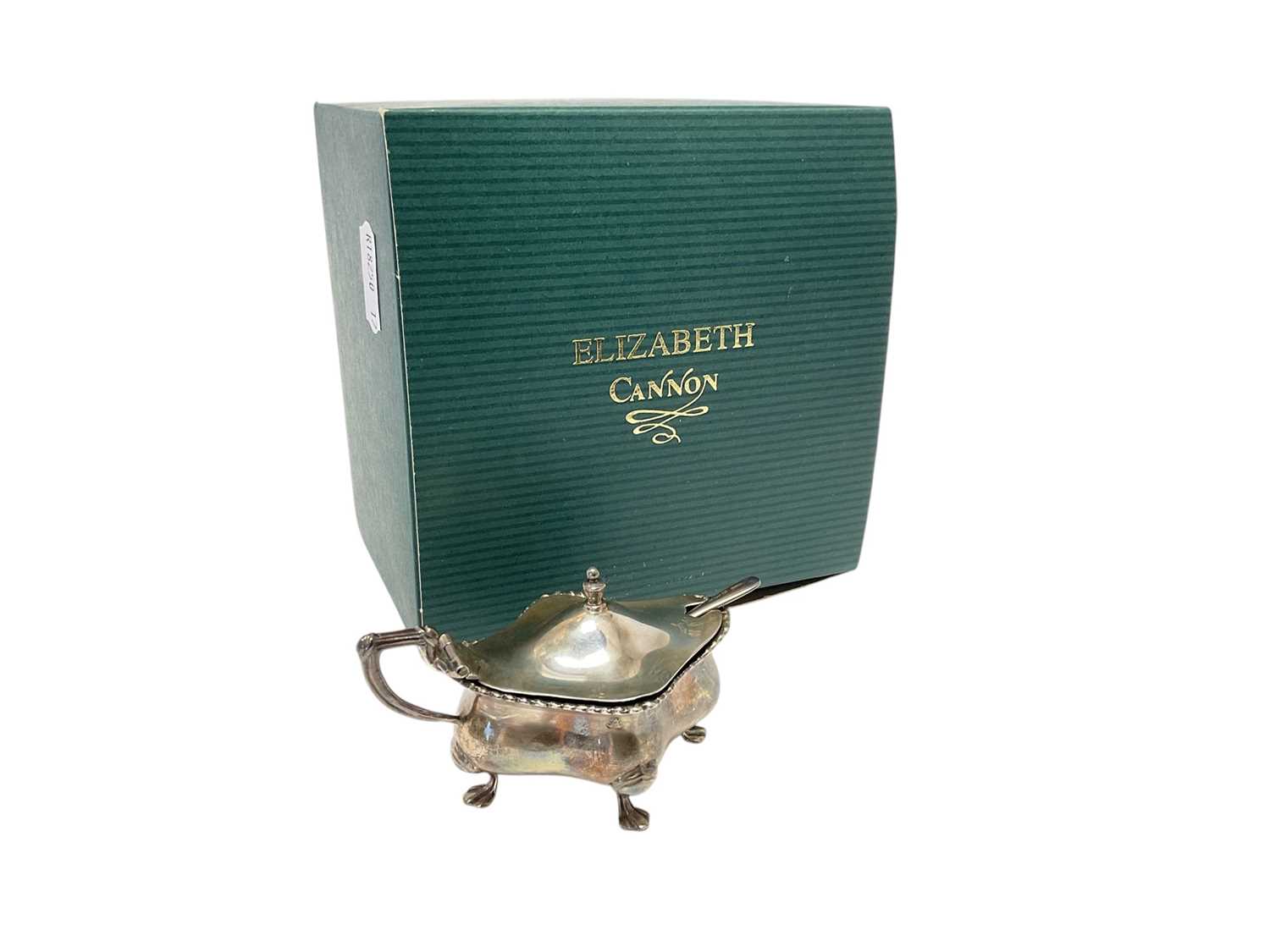Lot 225 - George V silver mustard pot of shaped form with blue glass liner, (Birmingham 1925), together with a silver spoon, in Elizabeth Cannon box.