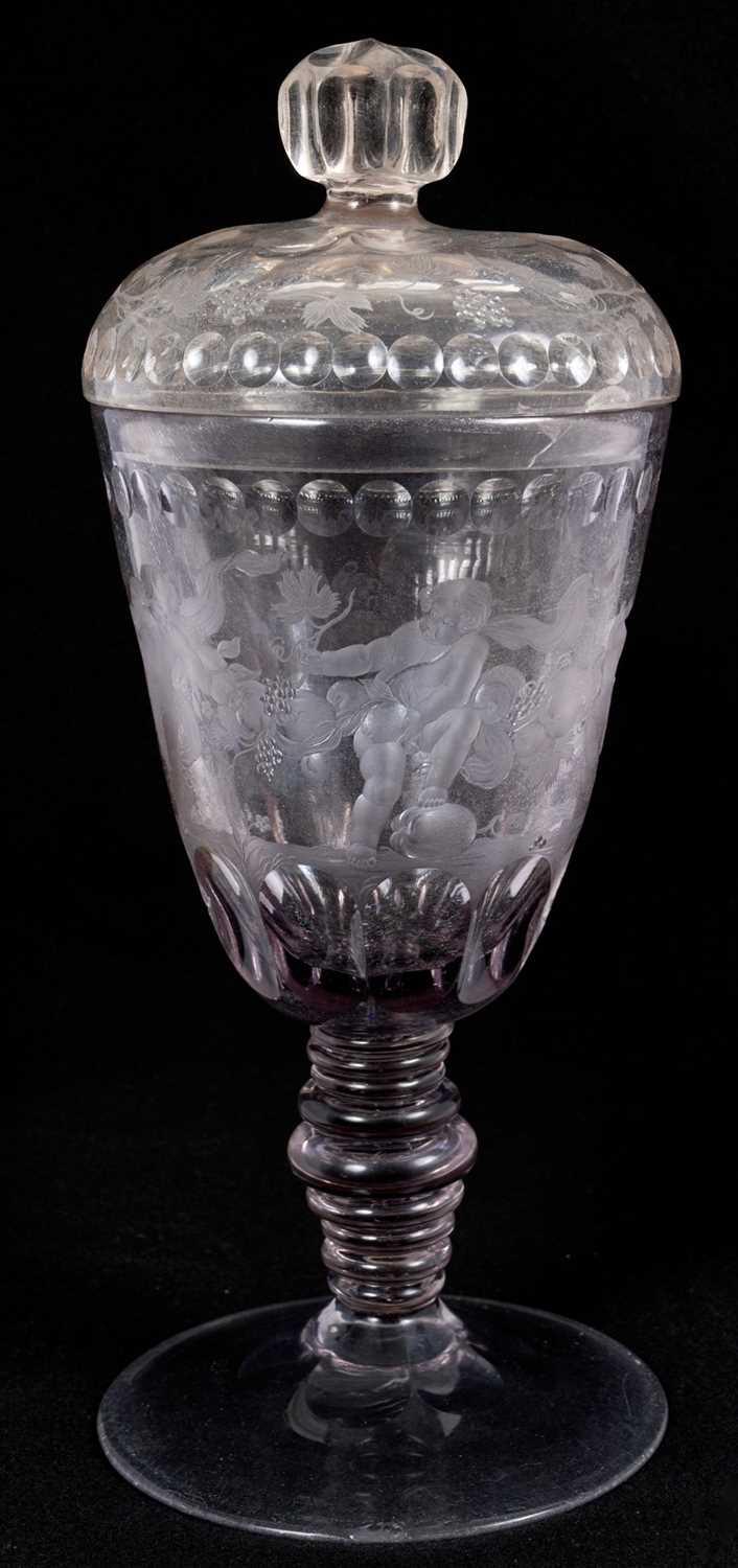 Lot 26 - Large Bohemian cut and engraved glass goblet and domed cover, circa 1730, well engraved with five putti around the body struggling with a heavy swag of pomegranates, grapes and other fruit, be...