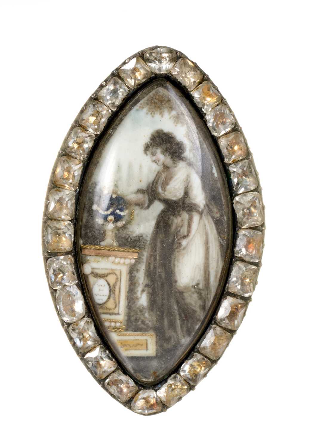 Lot 450 - George III mourning brooch of navette form, the ivory plaque painted in sepia depicting a lady standing by a gold and seed pearl urn on pedestal