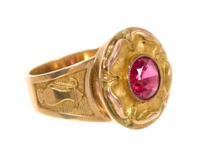 Lot 462 - Gold 'bishop' ring with stylised Tudor rose inset with a round mixed cut red stone, each tapered gold shoulder with an ecclesiastical ewer