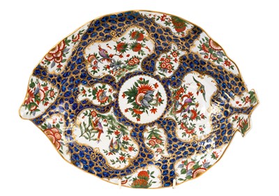 Lot 205 - A Worcester cabbage-leaf shaped dish, circa 1770, polychrome painted with panels of tropical birds and flowers, in gilt scroll borders on a blue scale ground, pseudo-Chinese mark, 31.5cm across<...