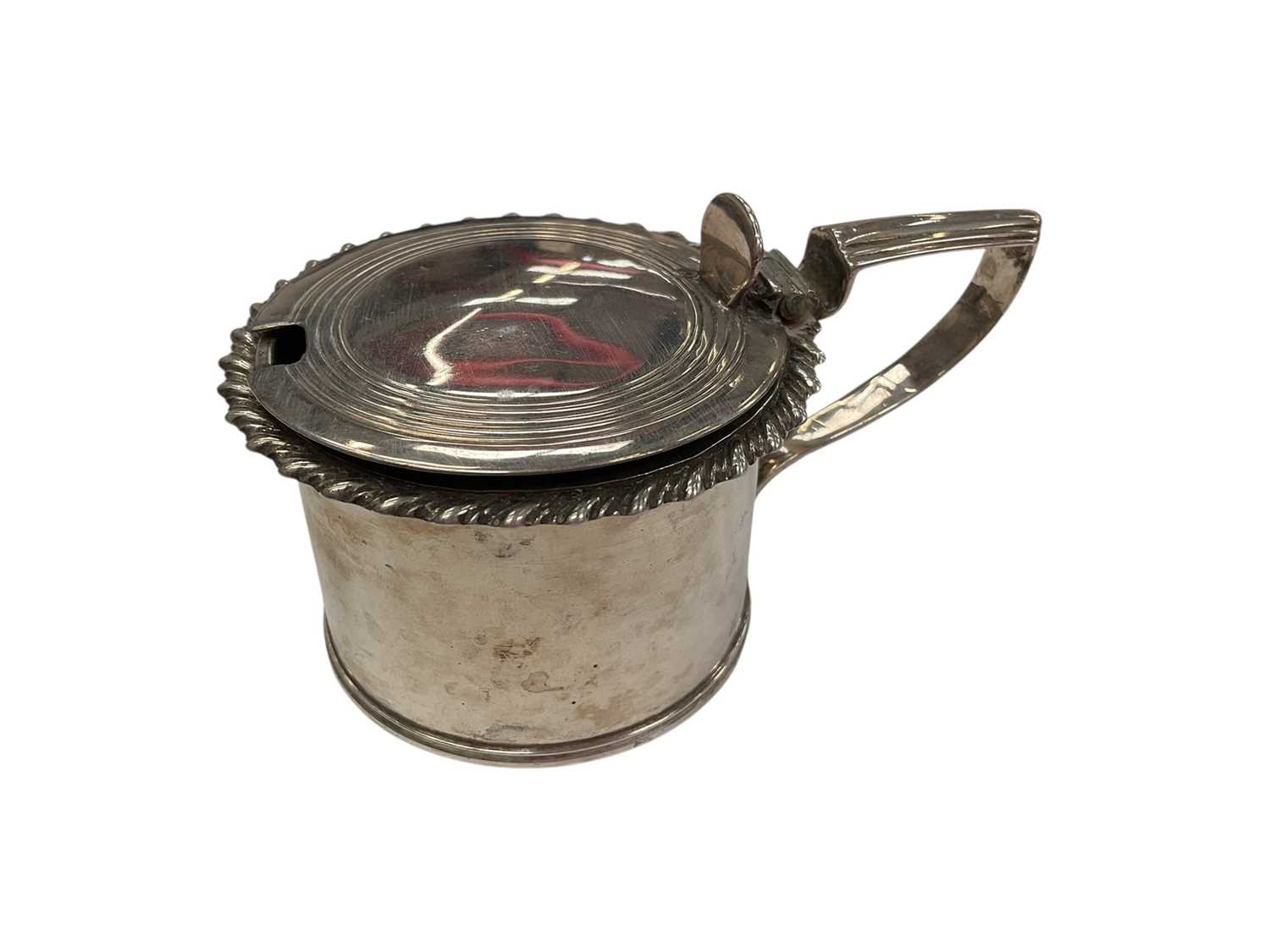 Lot 137 - Early Victorian silver mustard pot of drum form with gadrooned border, reeded angular handle and interior with blue glass liner, (London 1838), 5.1cm in overall height.