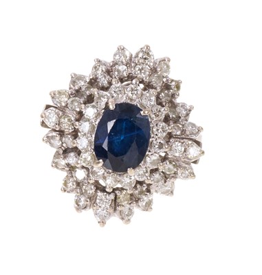Lot 705 - Sapphire and diamond cocktail ring an oval mixed cut blue sapphire measuring approximately 8.2mm x 6.5mm surrounded by fifty-six brilliant cut diamonds in undulating tiered claw setting on 18ct...