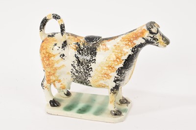 Lot 344 - An English creamware pottery cow creamer and stopper, circa 1800, with sponged decoration in ochre and black, the base painted green, 12.5cm high