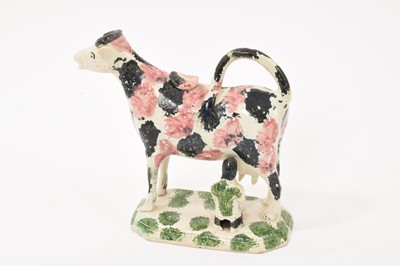 Lot 345 - An early 19th century English pearlware glazed pottery cow creamer and stopper, modelled with milkmaid, with pink, black and green splashed decoration, 14.75cm high