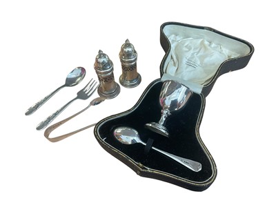 Lot 1134 - Silver christening egg cup and spoon in fitted case, pair of silver pepperettes with blue glass liners, pair of silver sugar tongs and a plated spoon and fork set