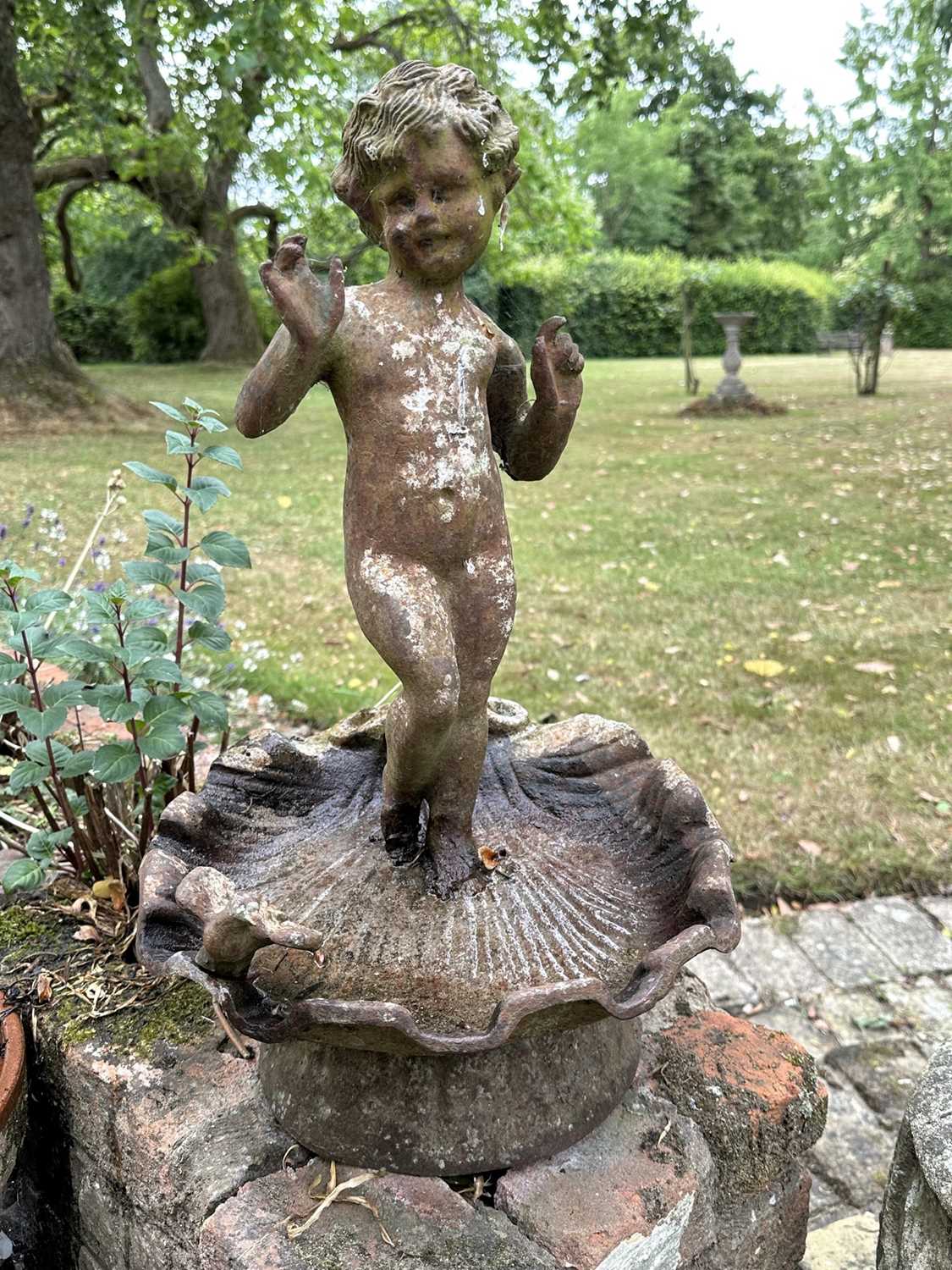Lot 1279 - Antique cast iron bird bath mounted with a putto standing with a shell, a bird to the rim, 56cm high