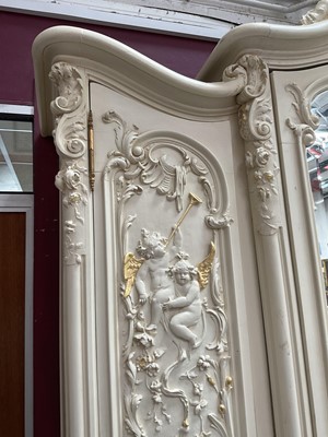 Lot 1353 - An impressive antique rococo revival wardrobe, the central mirrored doors enclosing five flanked by two cupboards, decorated with putti and foliate trailing decoration highlighted in gilt, on sc...