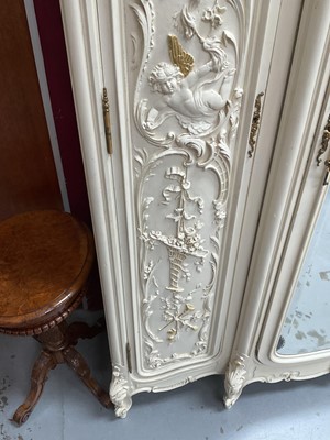 Lot 1353 - An impressive antique rococo revival wardrobe, the central mirrored doors enclosing five flanked by two cupboards, decorated with putti and foliate trailing decoration highlighted in gilt, on sc...
