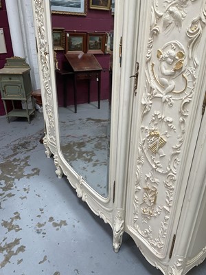 Lot 1353 - An impressive antique rococo revival wardrobe, the central mirrored doors enclosing five flanked by two cupboards, decorated with putti and foliate trailing decoration highlighted in gilt, on sc...