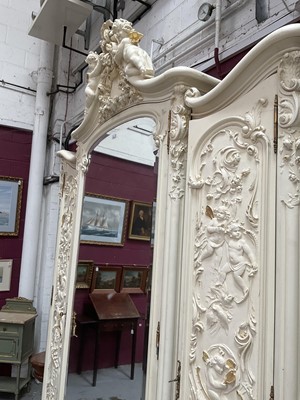 Lot 1353 - An impressive antique rococo revival wardrobe, the central mirrored doors enclosing five flanked by two cupboards, decorated with putti and foliate trailing decoration highlighted in gilt, on sc...