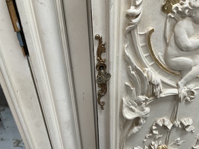 Lot 1353 - An impressive antique rococo revival wardrobe, the central mirrored doors enclosing five flanked by two cupboards, decorated with putti and foliate trailing decoration highlighted in gilt, on sc...