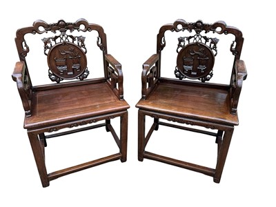 Lot 1380 - Pair of early 20th century Chinese hardwood elbow chairs, the backs decorated with central foliate panels surrounded by vining fruit, geometric formed arms, solid seats and square legs joined by...