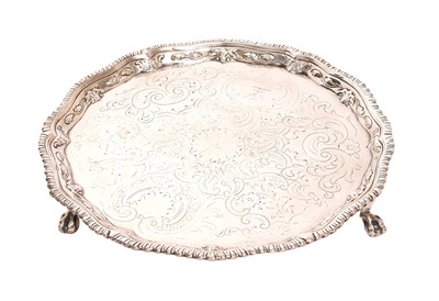 Lot 283 - George III silver salver, with gadrooned piecrust edge, cartouche with engraved family crest and repoussé rococo floral scrolls on three ball and claw feet, (London 1771)
