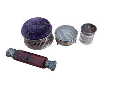 Lot 132 - Edwardian silver mounted pin cushion box, small silver jewellery box, silver and tortoiseshell mounted glass jar and a ruby glass double-ended scent bottle with white metal mounts (4)