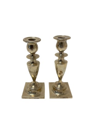 Lot 239 - Pair of Edwardian silver candlesticks, with tapered columns, beaded sconces and each raised on a square foot, (London 1902), maker Charles Boyton, each 19cm in overall height, (2).
