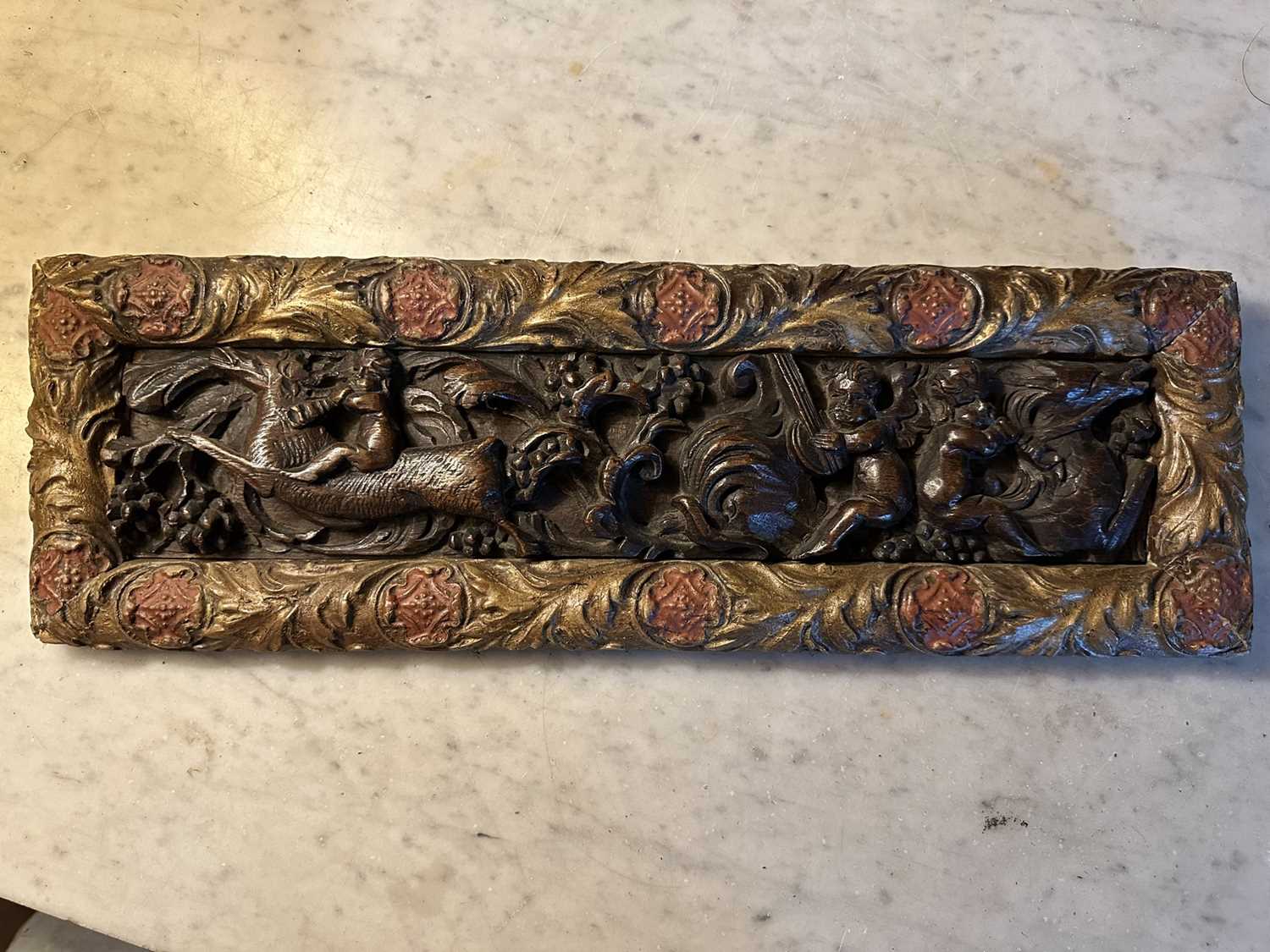 Lot 1510 - Antique, probably 17th century, carved oak frieze, depicting putto and mythical creatures, presented in a gilt and painted moulded frame, 15.5cm x 47.5cm