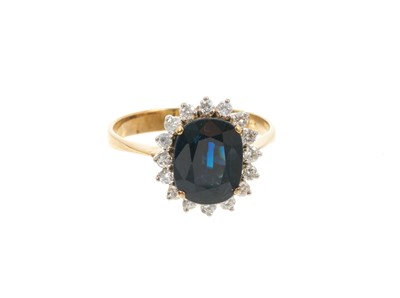 Lot 637 - Sapphire and diamond cluster ring with an oval mixed cut blue sapphire surrounded by a border of diamonds in claw setting on 14ct gold shank