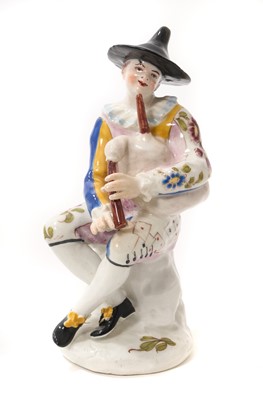 Lot 245 - Rare Longton Hall porcelain Harlequin figure, c.1755-60. Modelled after the Italian “Commedia dell’arte” character “Arlecchino”. The figure seated on a rock playing bagpipes, wearing a conical h...