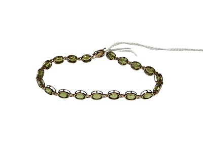 Lot 252 - 9ct gold peridot bracelet with a line of nineteen oval mixed cut peridots in 9ct gold rub over setting, 18.5cm