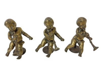 Lot 1875 - Set of three antique cast bronze cherubs, each wielding trumpets, raised on associated circular stands, 11cm high