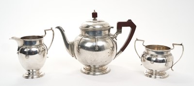 Lot 439 - George V three piece silver tea set, comprising teapot of compressed baluster form, with domed hinged cover and angular ebonised handle, raised on a circular foot, together with matching milk ju...