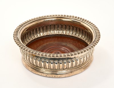Lot 454 - George III silver wine coaster, with fluted decoration, gadrooned border, and turned wood base, (London 1813), makers mark rubbed, 15.7cm in diameter.