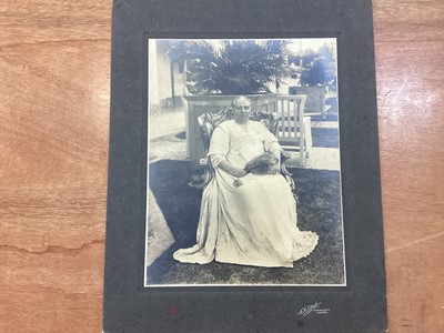 Lot 1208 - N.K. Otsubo Photographic Artist’s Singapore, an early 20th century large format photograph of a Singaporean Woman seated in a garden wearing finery and holding feather fan. Monogram lower left,...