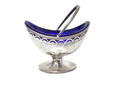 Lot 227 - George III silver sugar basket of navette form with pierced and engraved decoration, swing handle and blue glass liner to interior, (London 1791), 11.6cm in height (excluding handle).