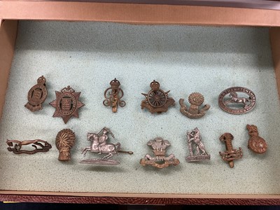 Lot 764 - Collection of fifty plus British Military cap badges and other badges to include Middlesex Volunteer Regiment, Northamptonshire Regiment, and The Royal Dragoons, housed in a four draw display ca...