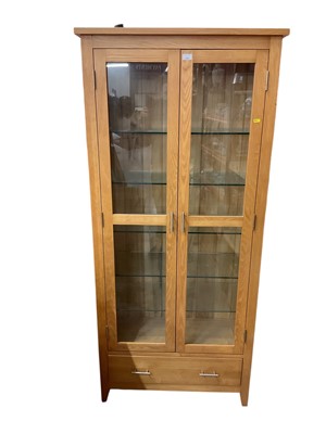 Lot 1302 - Contemporary light oak display cabinet enclosed with two glass doors, with drawer below.