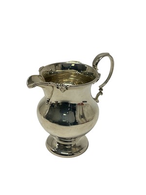 Lot 231 - 1920s silver cream jug of baluster form, with decorative rim and scroll handle, on a pedestal base