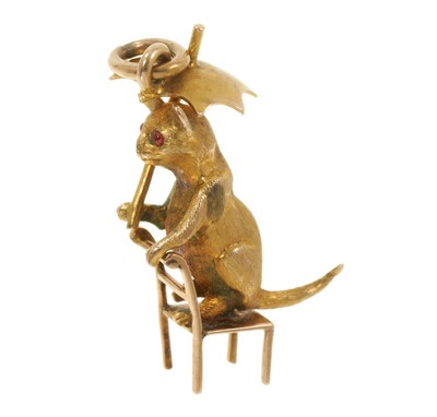 Lot 408 - Victorian yellow metal novelty cat charm with garnet cabochon eyes, standing on a backwards chair holding an umbrella