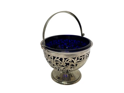 Lot 344 - Edwardian silver sugar basket with pierced decoration, swing handle and blue glass liner, raised on a pedestal foot, (Sheffield 1904), maker James Deakin & Sons, 9cm in height, (excluding handle.
