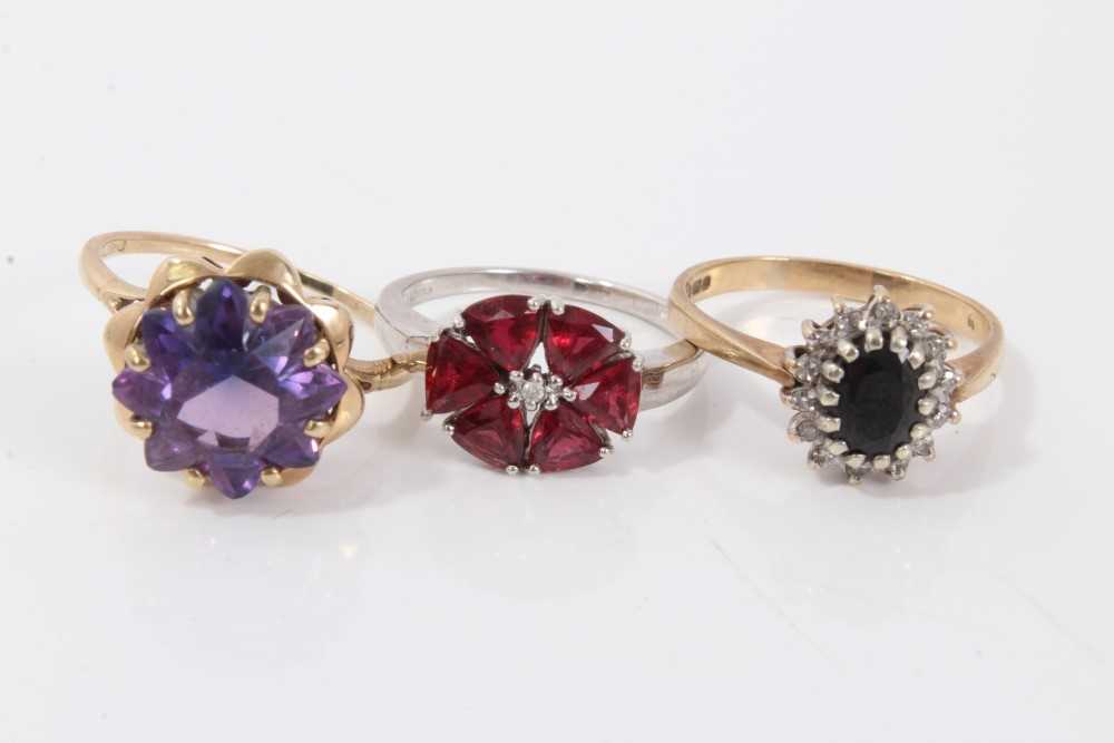 Lot 3229 - Two gold (9ct) gem set dress rings and a white gold (9ct) red stone flower head dress ring. (3)