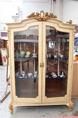 Lot 1400 - Continental cream painted display cabinet, arched form with pierced carved giltwood ribbon and floral cresting, enclosed by pair of glazed doors on cabriole legs, 146cm wide x 55cm deep x 225cm hig...