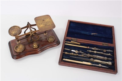 Lot 3820 - Set of late 19th/early 20th century brass postal scales, with four weights, on a wooden base, together with a cased set of drawing instruments. (2)