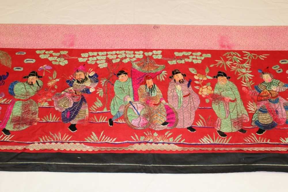 Lot 3054 - Chinese embroidered red silk banner. Silk satin stitch with crouched outlines, figures have painted silk faces, Wiseman in sedan chair, dancers and deities in garden scene. Printed cotton lining