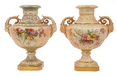 Lot 331 - Two Edwardian Royal Worcester blush ivory ground vases with moulded human mask handles, floral painted decoration on raised socle bases 23cm