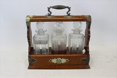 Lot 3636 - An oak three bottle tantalus, with metal mounts and handle, and glass bottles