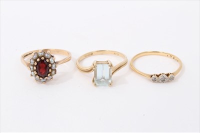 Lot 3445 - Three dress rings to include 18ct gold three stone diamond ring, 9ct gold aquamarine single stone ring and a 9ct gold garnet and seed pearl cluster ring (3)