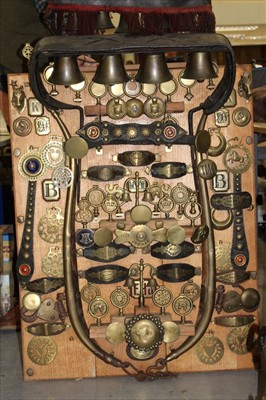 Lot 3795 - Superb mounted display board of antique horse brasses and tack, surmounted by bar of five bells, an arrangement of straps, terrets and ornamental brasses below