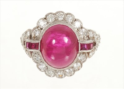 Lot 494 - Ruby and diamond cocktail ring with an oval cabochon ruby estimated to weigh approximately 7cts, flanked by calibre cut rubies to the shoulders with brilliant cut diamonds to the oval border and bi...