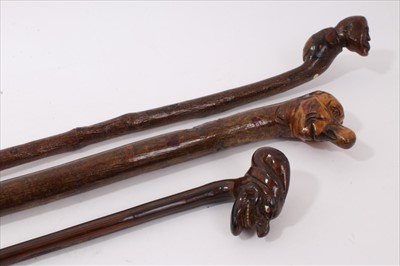 Lot 720 - 19th century grotesque exotic wood walking stick, the terminal carved with a grinning head, with glass eyes and bone teeth, 80cm long, together with two further sticks with carved head terminals