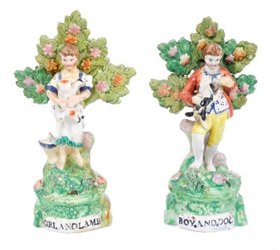 Lot 70 - Charming pair of Staffordshire pearlware figures, circa 1820, showing a boy and girl with a dog and lamb, standing on grassy mounds with bocage behind them, with titles at the bottoms