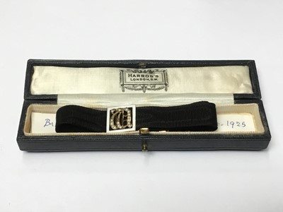 Lot 181 - 1920s black silk bracelet with 9ct gold enamel and seed pearl panel with gothic initial with gold clasp, in original Harrods box with note 'Bridesmaid's present KGS-ENH Dec.1925'