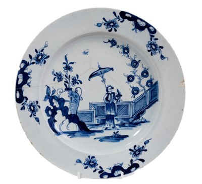 Lot 50 - A good Lowestoft blue and white plate c.1770, painted with a Chinese lady holding a parasol, standing before a zigzag fence, the rim with three vignettes of prunus issuing from rockwork, 23cm